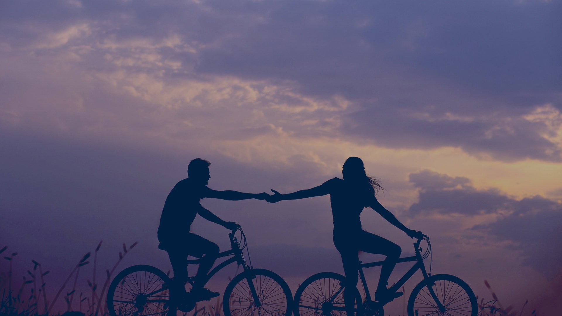 two people holding hands while riding bikes during purple dusk
