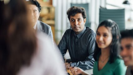 Group of professionals sitting around a conference table, listening attentively in a collaborative meeting.