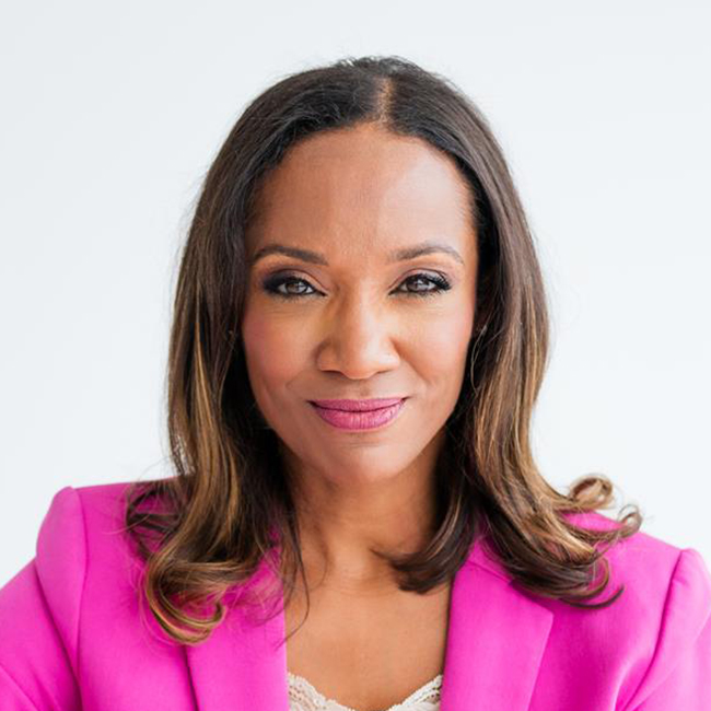 A confident woman with long brown hair wearing a bright pink blazer and cream lace top, smiling slightly against a plain white background
