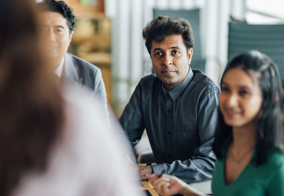 Group of professionals sitting around a conference table, listening attentively in a collaborative meeting.