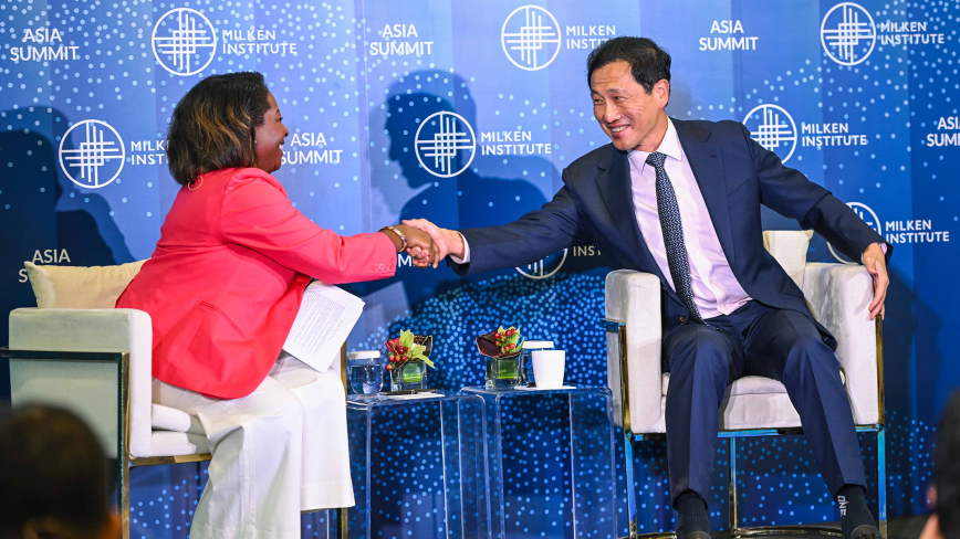 An image of a woman named Esther Krofah and a man named Ong Ye Kung. They are shaking hands and sitting on a stage at the Milken Institute's Asia Summit 2024 in front of a blue Milken Institute backdrop. Ong Ye Kung is Asian in appearance and has short black hair, white skin, and is wearing a navy blue suit with a blue tie. Esther Krofah has brown skin, short brown hair, and is wearing a hot pink blazer with white dress pants.