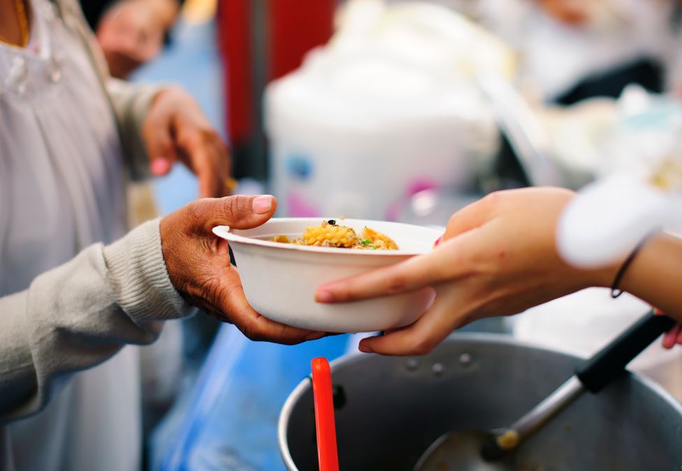 An image of someone's hands, handing over a bowl of food to another person's hands.