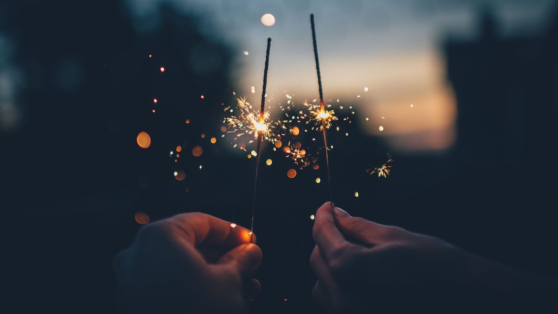 two hands holding up sparklers at twilight