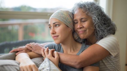 An older woman hugging a younger woman sitting against a couch