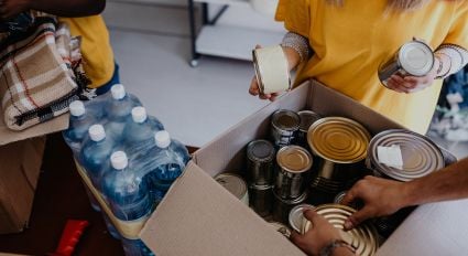 A person packs cans and supplies in a cardboard box