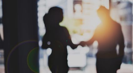 The silhouettes of two individuals shaking hands