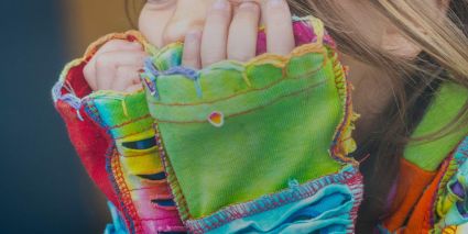 A child's hands by their face wearing a colorful long sleeve shirt