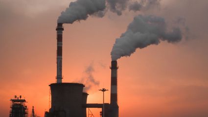 Two smoke stacks releasing smoke against a sunset sky