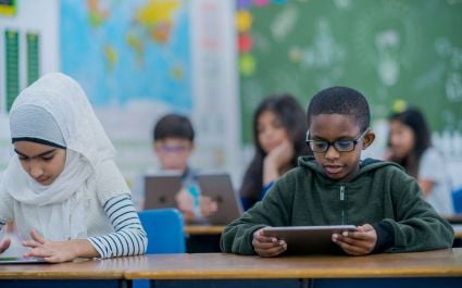 A few schoolkids sitting at their desks with tablets in their hands