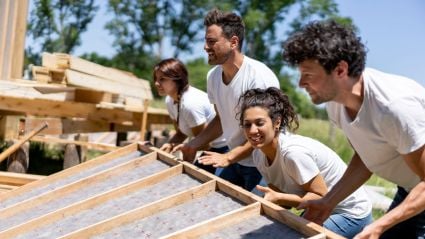 Four people erecting a wooden wall while building a house.