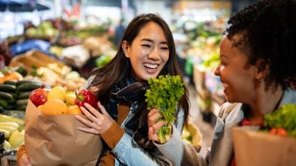 Two smiling women shop for groceries in the produce section