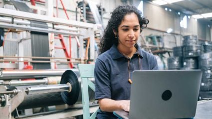 A female worker standing at a desk with a computer in a manufacturing setting