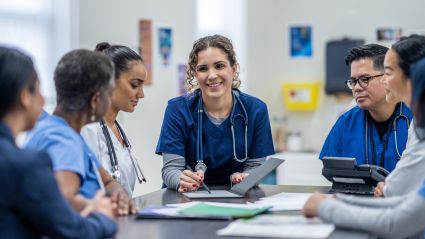 A doctor speaks to other health care workers at a table.