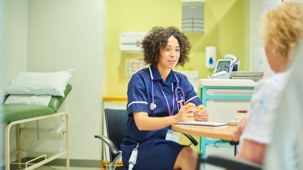 medical professional with dark curly hair sitting at desk talking to patient