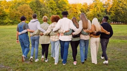 An image of a group of people, facing their backs. They are a diverse group of adult people walking with their arms around each other through a field, leading to an article from the Milken Institute titled "How Philanthropy Can Support a Community-Centered Biomedical Research Ecosystem to Achieve Health Equity".