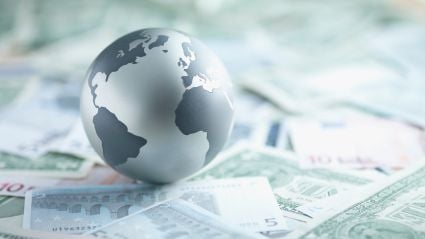 An image of a grayscale globe of Earth sitting upon various paper currencies.