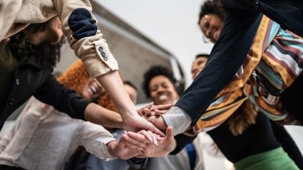 An image of a diverse group of people all putting their hands together in a circle.