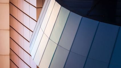 Close-up of a modern building with reflective angled panels in shades of blue and beige.