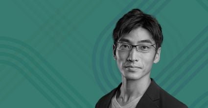 Portrait of a man with short dark hair and glasses, wearing a blazer over a T-shirt, on a teal background with the Milken Institute logo in the top left corner.