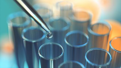 Pipette dispensing a liquid droplet into a row of laboratory test tubes.