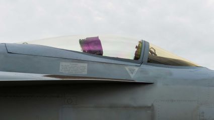 Close-up side profile of a grey fighter jet’s cockpit canopy against a cloudy sky.