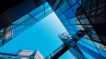 Upward view of modern glass skyscrapers reflecting a clear blue sky.