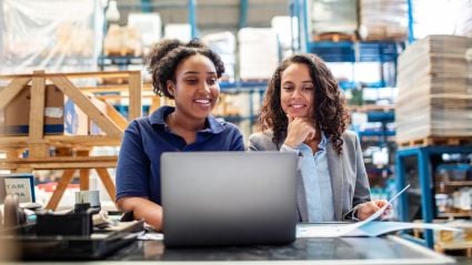 Two women working together at a laptop in a warehouse storage facility