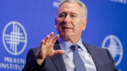 Ken Griffin speaking at Milken Institute event, gesturing with hand against blue background