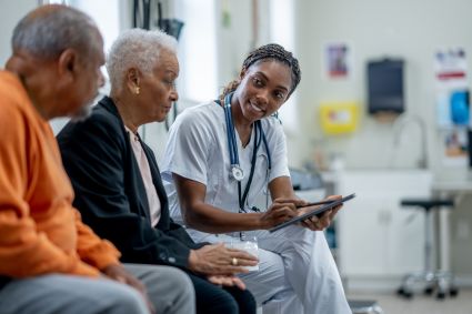 Healthcare worker showing tablet to two elderly patients in medical waiting room