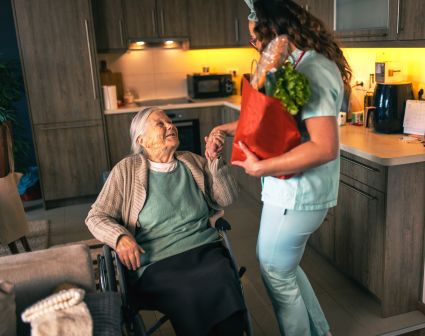 Woman presenting flowers to elderly woman seated in kitchenette 