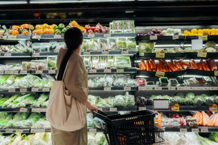 Woman with shopping basket browsing fresh produce aisle in grocery store