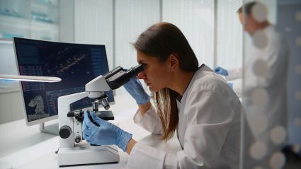 Scientist in white lab coat looking through microscope in laboratory