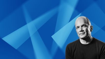 Man in black shirt smiling against blue geometric background