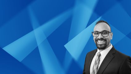 Professional headshot of smiling man in suit and glasses against blue geometric background