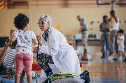 Healthcare worker in white coat kneeling while assisting a young child
