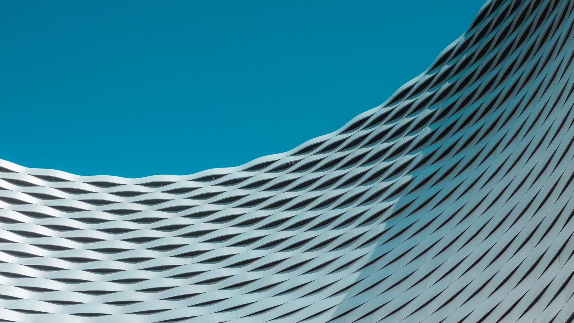 A white geometric architectural structure curves across the image against a blue sky