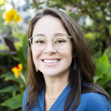 Female-presenting person with brown hair, wearing a blue shirt against a floral background