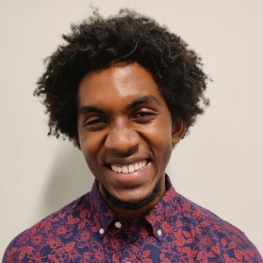 Smiling darker-skinned, male-presenting person wearing a floral button up