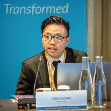 Male-presenting person of Asian heritage speaking into a microphone with a teal blue backdrop