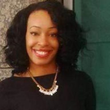 A smiling darker-skinned female with short black hair wearing a black shirt against an ambiguous background