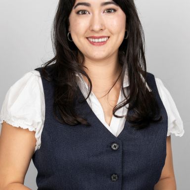 A woman wearing a white shirt and navy vest against a light background.