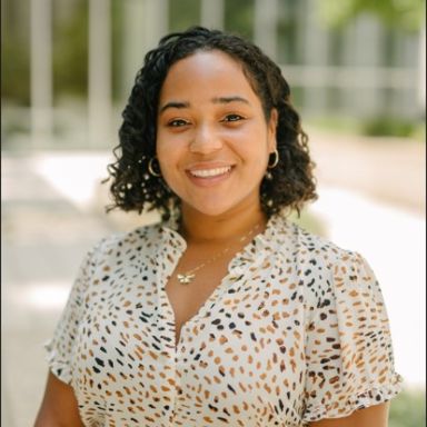 A smiling woman in a light blouse against an outdoors background.
