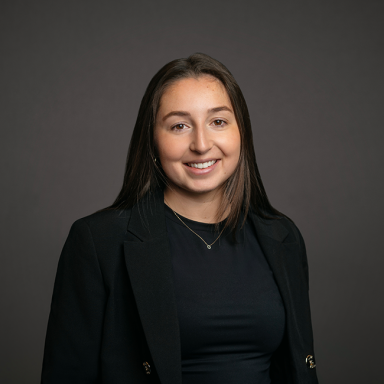 Professional headshot of Erin Cieslewski, a woman with straight brown hair, wearing a black top and black blazer. She is smiling softly and posed against a dark gray background.