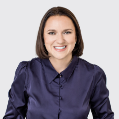 Professional headshot of a smiling woman in a navy blue button-down shirt against white background