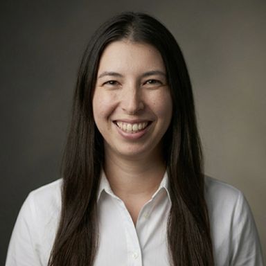 Professional headshot of smiling woman with long dark hair wearing white collared shirt