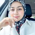 A smiling light-skinned woman of Asian heritage wearing a white shirt and a headscarf