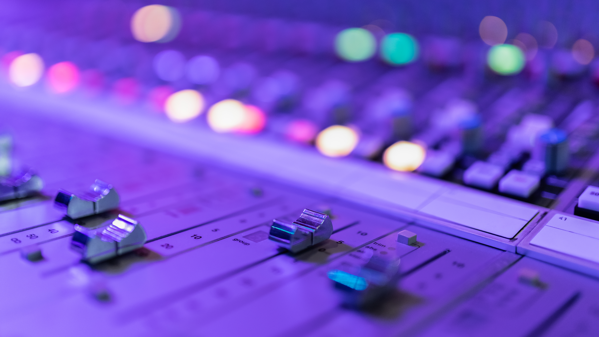 Audio mixing console with faders bathed in purple and blue lighting