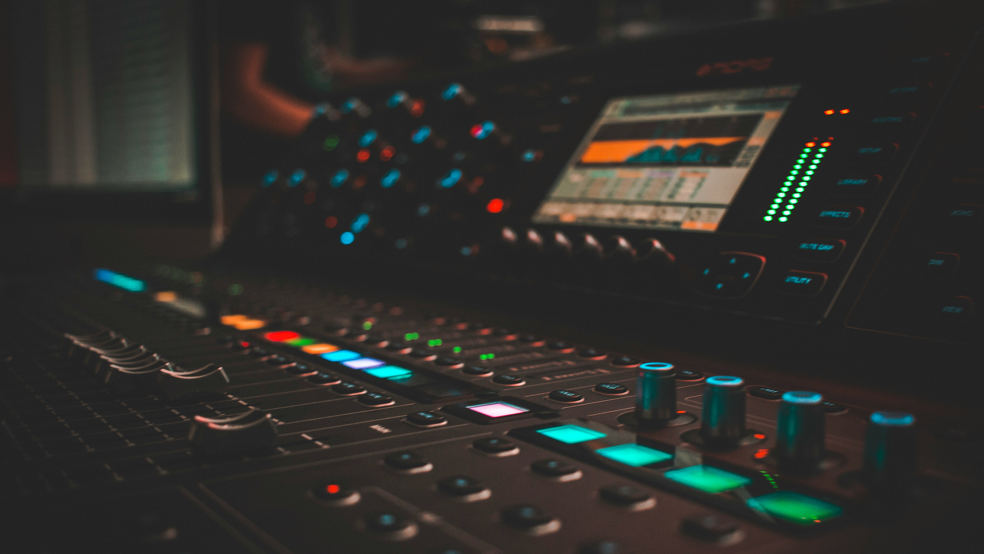 Audio mixing console with illuminated controls in a dimly lit studio