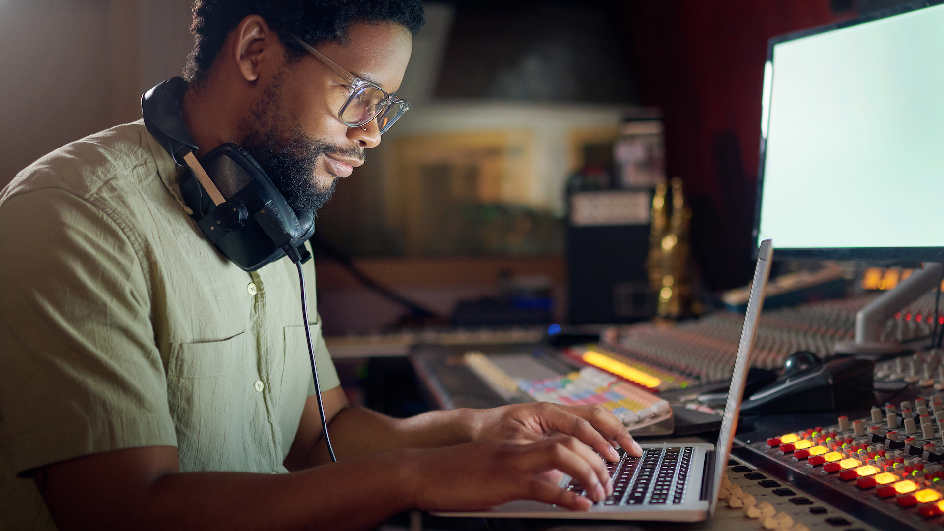 Man wearing glasses working on laptop at desk in dimly lit room