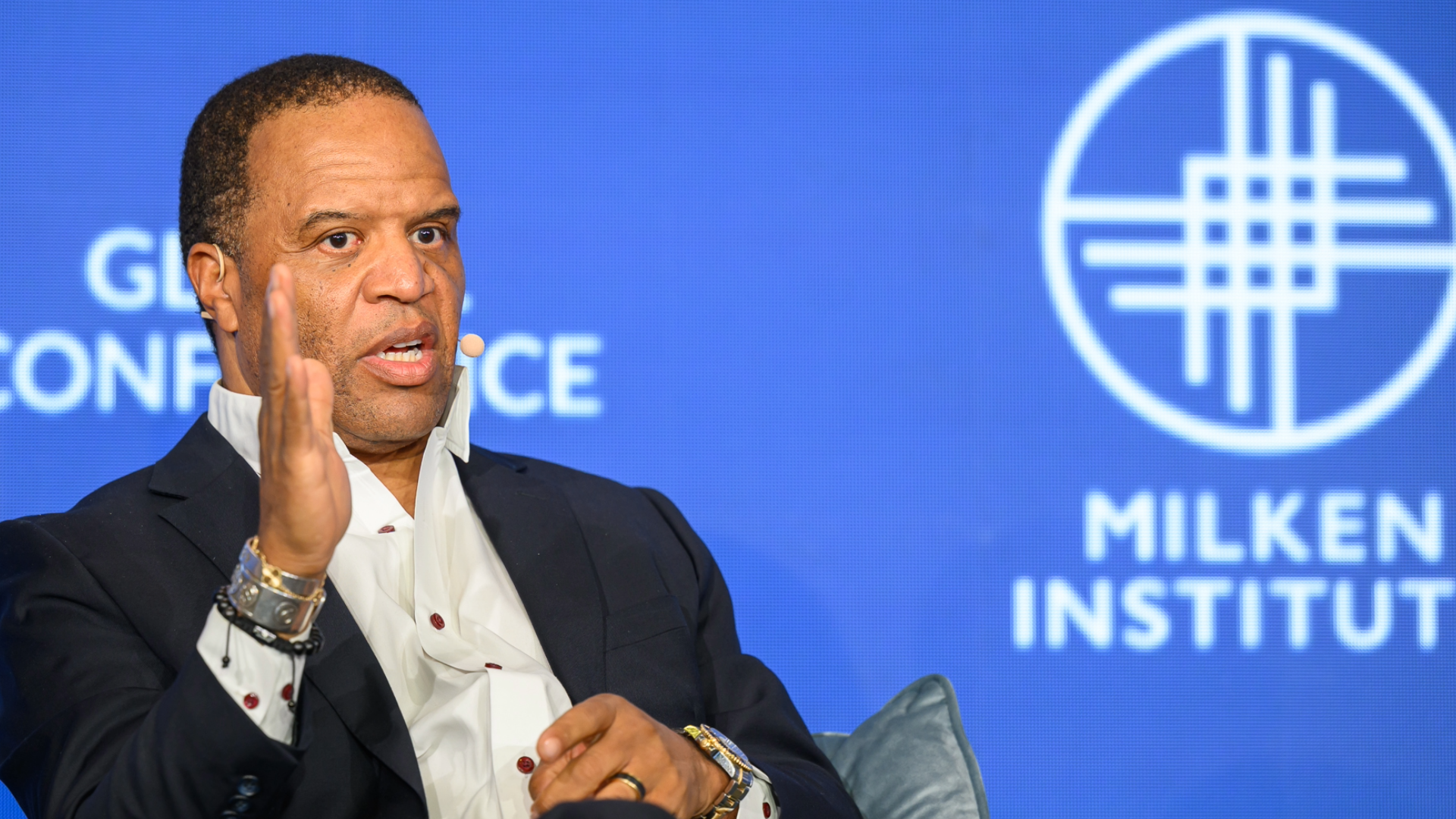 John Hope Bryant speaking at Milken Institute event with blue backdrop